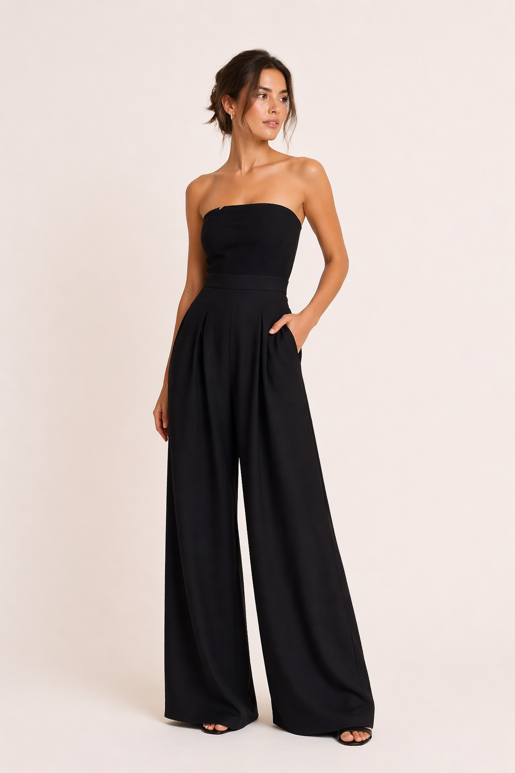 Elegante dames strapless jumpsuit met wijde pijpen in zwart, gedragen door model met opgestoken haar en hand in zak.