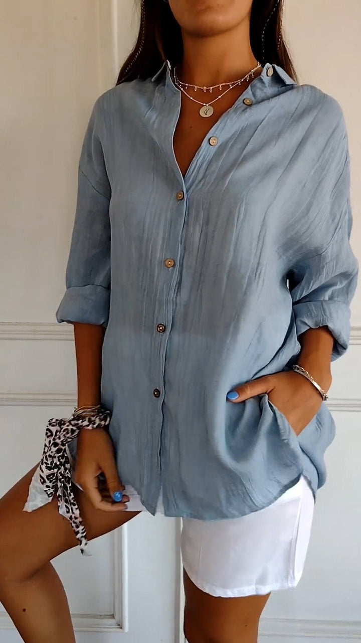 Elegante damesblouse Naya in crème, nauwsluitend en van fijn materiaal voor feestelijke gelegenheden, op een grijze achtergrond.