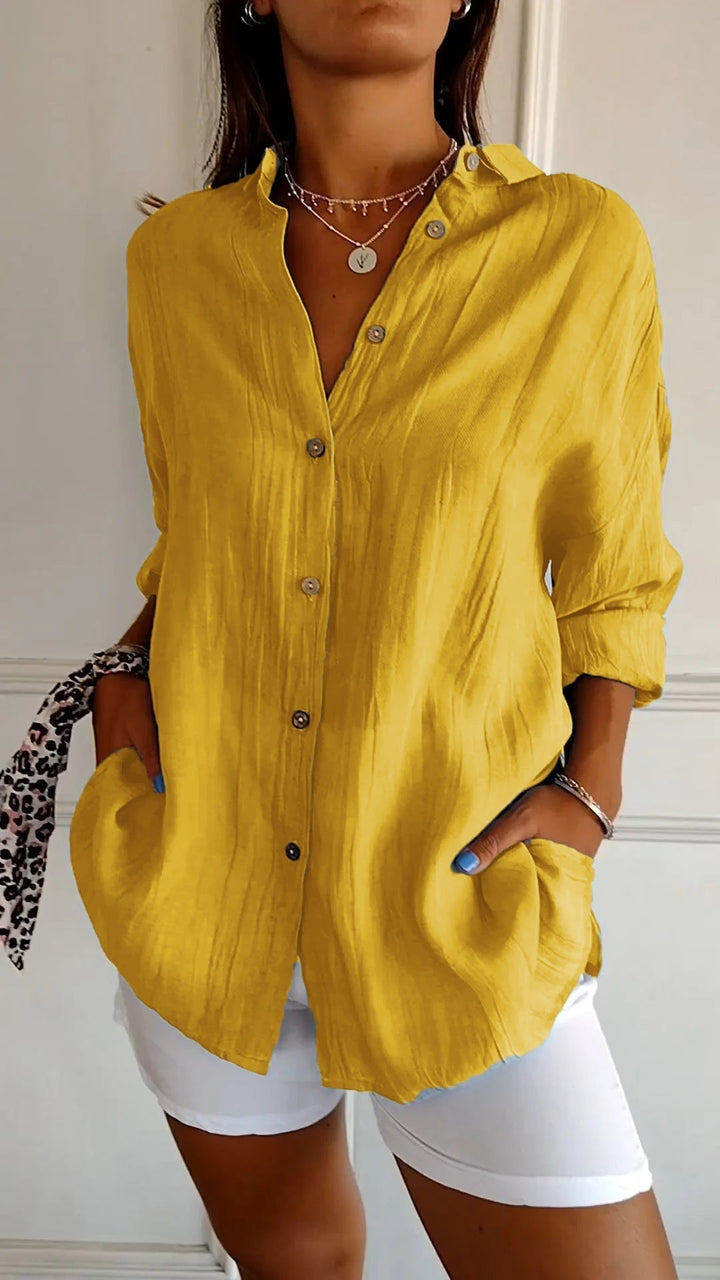 Elegante damesblouse Naya in crème, nauwsluitend en van fijn materiaal voor feestelijke gelegenheden, op een grijze achtergrond.