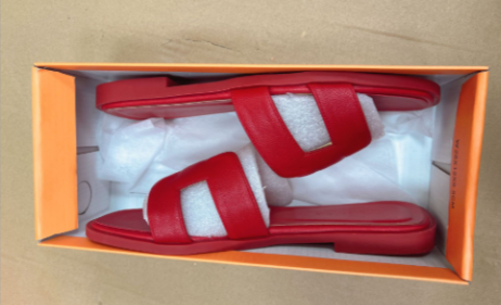 Damesmodel draagt de Hermes geïnspireerde rood-zwarte sandalen.