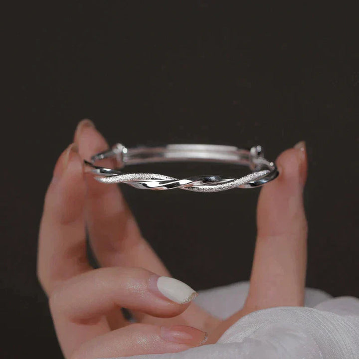 Close-up van een gedraaide zilverkleurige damesarmband, met gedetailleerd en elegant design.