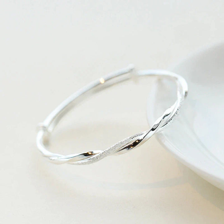 Zilverkleurige gedraaide damesarmband elegant gedragen om de pols, een verstelbaar fashion sieraad.