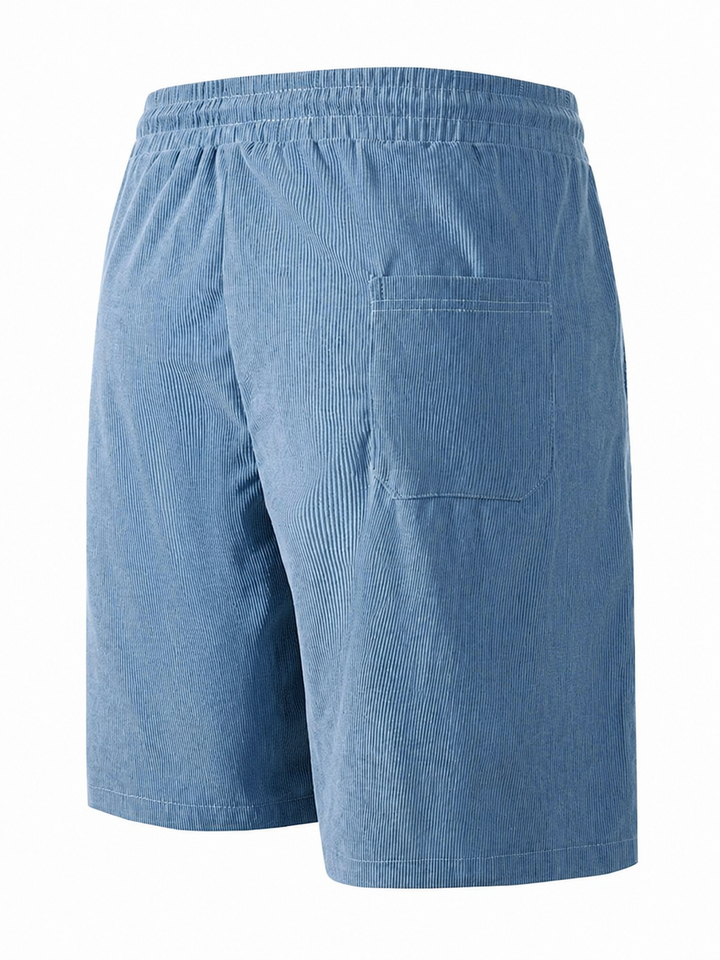 Man staat met handen in de zakken van de relaxte heren shorts in beige kleur