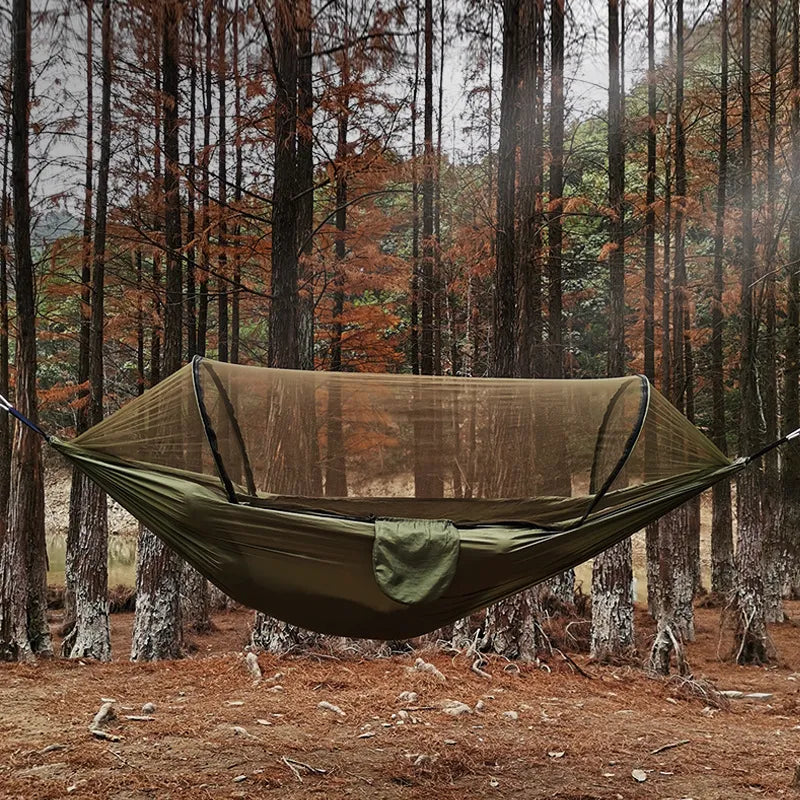 Outdoor hangmat met muskietennet, gemaakt van groene parachutestof, hangend tussen twee bomen, ideaal voor kamperen.