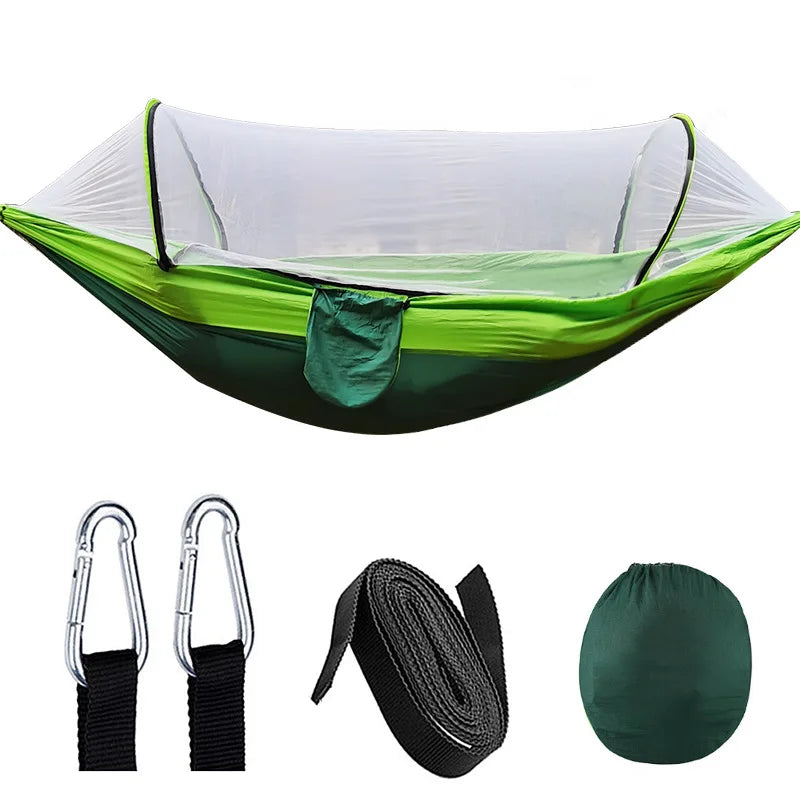 Outdoor hangmat met muskietennet, gemaakt van groene parachutestof, hangend tussen twee bomen, ideaal voor kamperen.