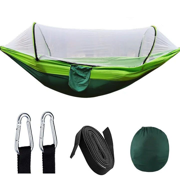 Outdoor hangmat met muskietennet, gemaakt van groene parachutestof, hangend tussen twee bomen, ideaal voor kamperen.