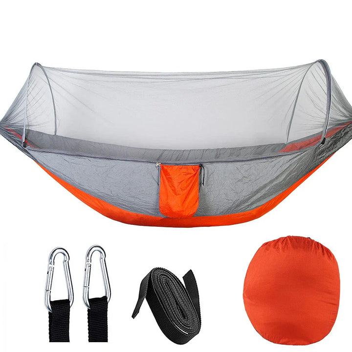 Outdoor hangmat met muskietennet, gemaakt van groene parachutestof, hangend tussen twee bomen, ideaal voor kamperen.