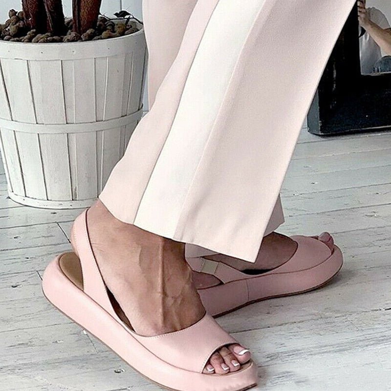 Roze zomersandaal voor dames met een elastisch slip-on ontwerp en lage hak op een grijze achtergrond.