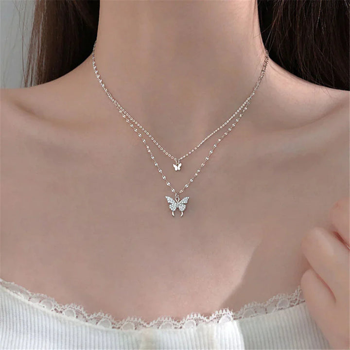 Duo-laags zilveren ketting met vlinderhanger en sprankelende zirkoniastenen, elegant en natuur-geïnspireerd sieraadontwerp.