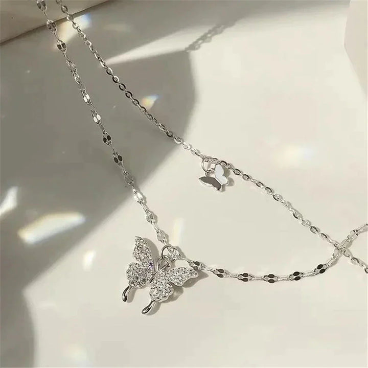 Duo-laags zilveren ketting met vlinderhanger en sprankelende zirkoniastenen, elegant en natuur-geïnspireerd sieraadontwerp.
