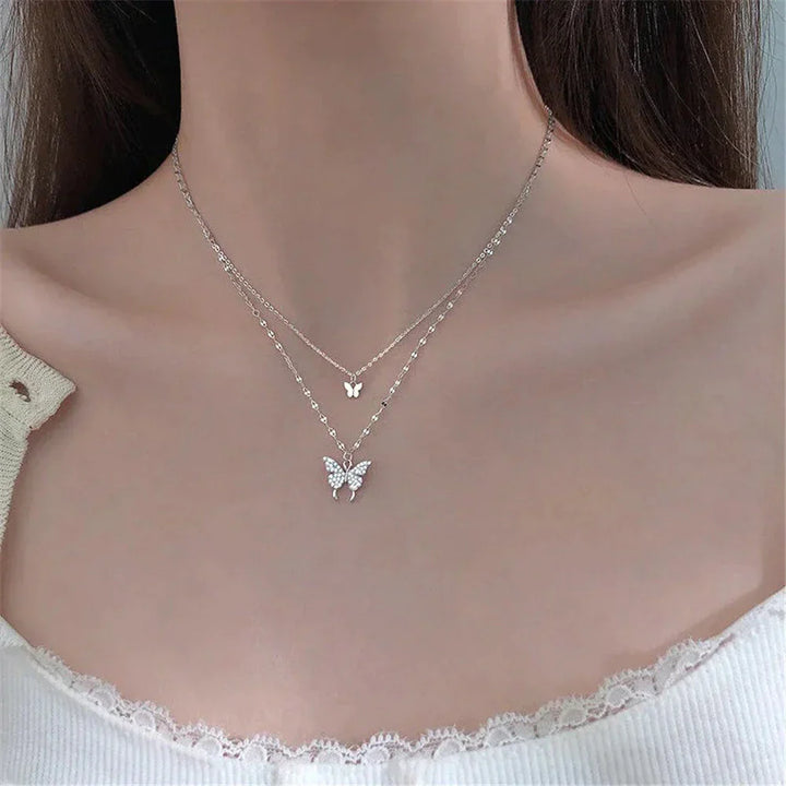 Duo-laags zilveren ketting met vlinderhanger en sprankelende zirkoniastenen, elegant en natuur-geïnspireerd sieraadontwerp.