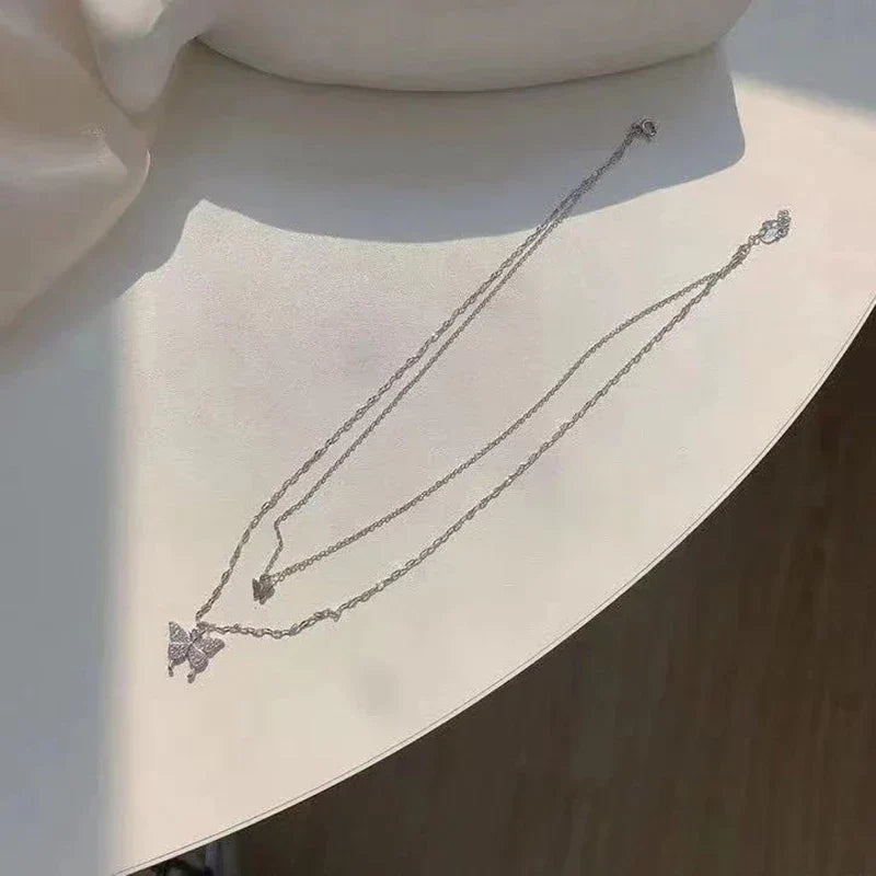Duo-laags zilveren ketting met vlinderhanger en sprankelende zirkoniastenen, elegant en natuur-geïnspireerd sieraadontwerp.